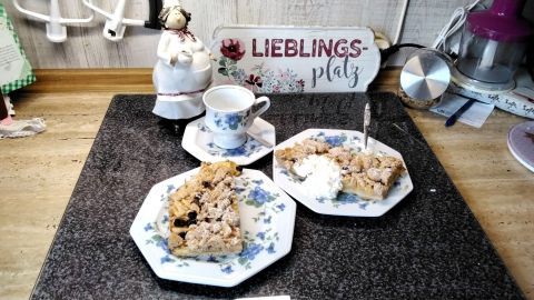 Zwei Stück Apfelstreuselkuchen mit Rosinen liegen auf einem gedeckten Tisch, neben einer Tasse und einer dekorativen Figur.
