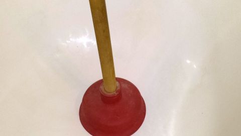 Ein Pömpel steht in einem weißen Abflussbecken. Er wird zur Reinigung des Abflusses verwendet.