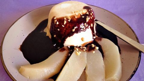 Eine weiße Mousse au Chocolat mit einer glänzenden Schokoladensauce auf einem Teller, zusammen mit Birnenscheiben.