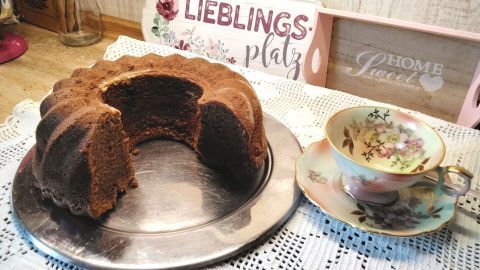Ein klassischer Eierlikörkuchen steht auf einem silbernen Teller, umgeben von einem rustikalen Küchentisch und einer blumigen Teetasse.