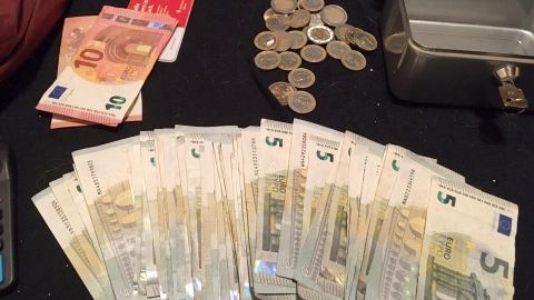 Staples of cash, including various Euro bills and coins, are neatly arranged on a surface next to a small lockbox.