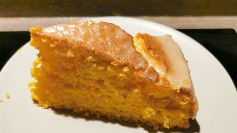 Ein saftiges Stück Karottenkuchen mit Mandeln liegt auf einem weißen Teller, umgeben von einem dunklen Holzuntergrund.