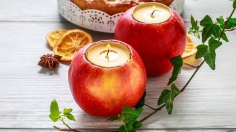Roten Äpfel mit Kerzen stehen auf einem Holztisch, umgeben von Deko, bereit für stimmungsvolle Herbstdeko.