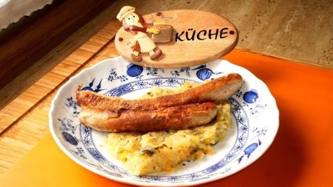 Zwei braune, panierte Bratwürste liegen auf einem Teller mit Sauerkraut, umgeben von einer rustikalen Küchendekoration.