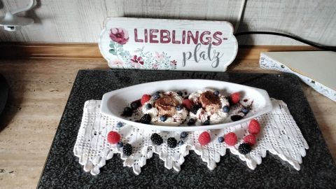 Ein Winter-Parfait liegt dekorativ auf einem weißen Teller, umgeben von frischen Beeren und einem gehäkelten Tischläufer.