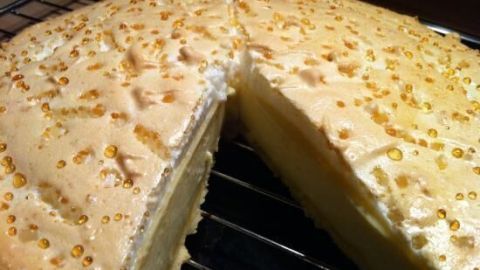 Eine goldene Käsekuchen-Torte mit glatter Oberfläche und leichten Zuckerkristallen, angeschnitten und auf einem Gitterrost platziert.