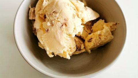 Ein cremiger Kinder Bueno-Eis-Scoops liegt in einer schlichten Schüssel auf einem weißen Tisch.