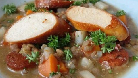 Eine herzhafte Linsensuppe mit Weißwürsten und frischem Gemüse, garniert mit Petersilie und Brezenstücken.