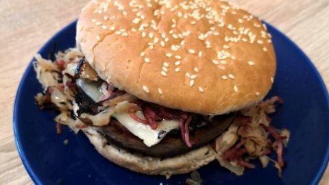 Ein Dosenwurstburger liegt auf einem blauen Teller und enthält Wurst, Käse und Kraut zwischen zwei Brötchenhälften.