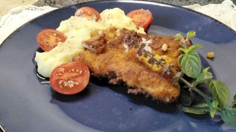 Saftige Putenschnitzel liegen auf einem blauen Teller, begleitet von pürierten Kartoffeln und frischen Tomatenscheiben.