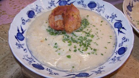Eine cremige Blumenkohlsuppe mit knusprigem Blumenkohlstück im Zentrum, umgeben von frischem Schnittlauch auf schönem Geschirr.