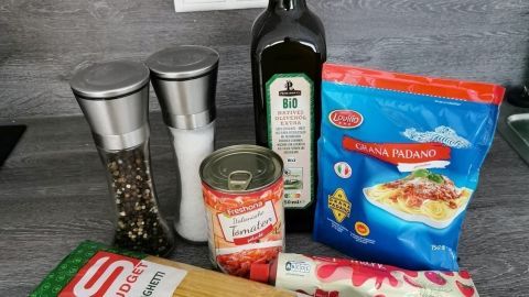 Ein Paket Spaghetti und Tomatensoße stehen auf einem Küchentisch neben Olivenöl und Gewürzen, bereit zum Kochen.