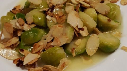 Rosenkohl wird mit gerösteten Mandeln angerichtet und liegt auf einem weißen Teller in einer appetitlichen Anordnung.