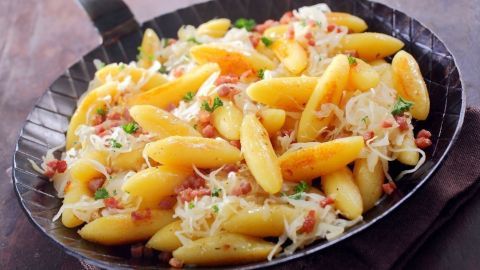 Eine gebräunte Pfanne mit herzhaften Spätzle, Sauerkraut und Speckstückchen, serviert auf einem rustikalen Holzuntergrund.