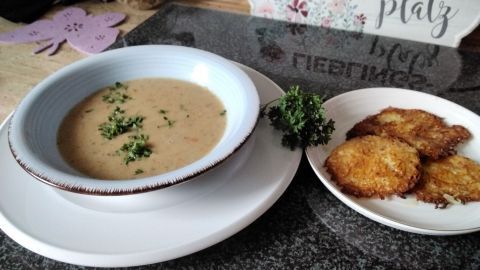 Eine cremige Kartoffelsuppe mit frischer Petersilie steht in einer Schüssel, neben knusprigen Kartoffelpuffern auf einem Teller.