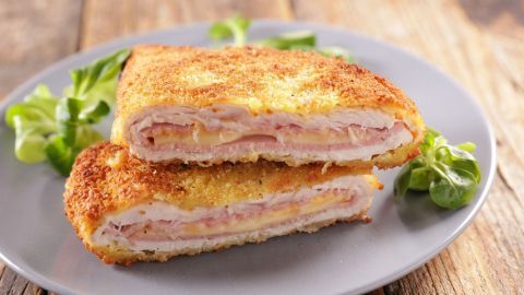 Knusprige Cordon bleu-Stücke liegen auf einem grauen Teller, umgeben von frischen Salatblättern.