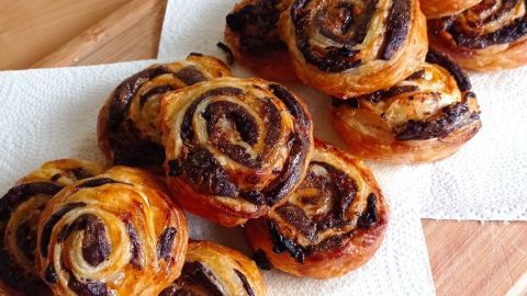 Blutwurst-Blätterteig-Schnecken liegen auf Küchenpapier, knusprig und spiralförmig, frisch aus dem Ofen.