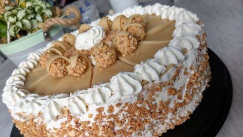 Eine dekorative Giotto-Torte mit Sahne, Nüssen und Schokoladenstücken steht auf einem schwarzen Teller in einem hellen Raum.