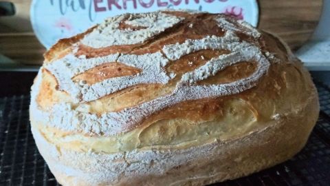 Ein frisch gebackenes Brot liegt auf einem Abkühlgitter, während im Hintergrund ein dekoratives Schild steht.