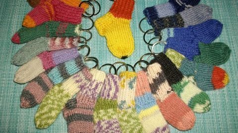 Bunte Mini-Socken auf Schlüsselringen angeordnet, mit einer zentralen gelben Socke, auf einem türkisfarbenen Hintergrund.