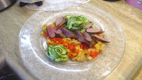 Auf einem eleganten Teller liegt zarte Schweinelende, kleingeschnitten, umgeben von frischem Salat und Gemüse.