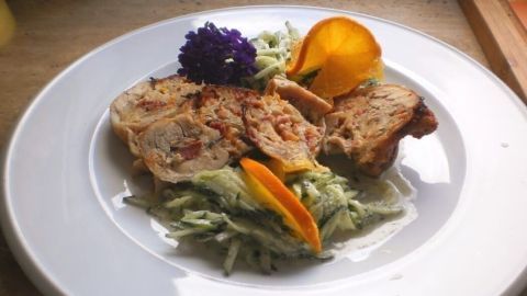 Gefüllte Hähnchenschenkel sind auf einem weißen Teller angerichtet, dazu frischer Salat und dekorative Orangenscheiben.