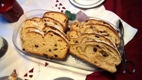 Scheiben von Marzipanstollen aus Hefeteig liegen auf einem Teller, umgeben von festlicher Tischdekoration und Geschirr.