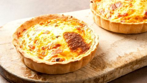 Zwei goldbraune Quiches auf einem Holzbrett, frisch gebacken und appetitlich, bereit zum Servieren als Lachs-Gemüse-Gericht.