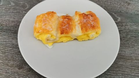 Auf einem weißen Teller liegt ein gebackenes Puddingteilchen aus Blätterteig, goldbraun und gefüllt mit cremiger Vanillefüllung.