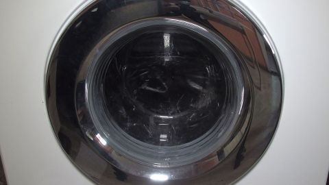 Die Waschmaschine öffnet die Tür, um Wäsche einzuladen, und steht vor einer weißen Wand in einem modernen Raum.