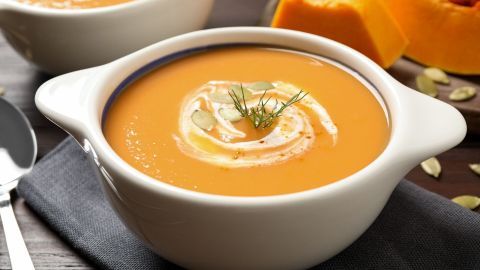 Eine cremige Kürbiscremesuppe wird in einer weißen Schale serviert, umgeben von frischen Kürbisstücken und Kerne.