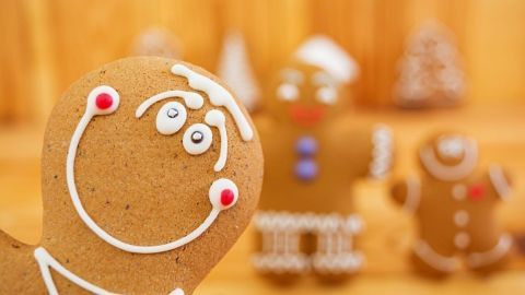 Ein fröhlicher Lebkuchenmann mit buntem Zuckerguss lächelt, während andere Kekse im Hintergrund stehen, umgeben von Holz.