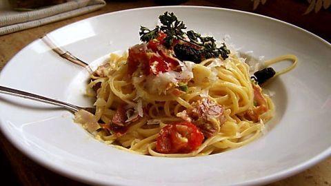 Eine Spaghetti-Pfanne mit Tomaten und Kräutern wird appetitlich auf einem weißen Teller angerichtet, umgeben von einem gemütlichen Ambiente.