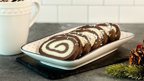 Kokos-Rum-Rollen liegen ordentlich auf einer Platte, umgeben von einer Kaffeetasse und winterlicher Dekoration.