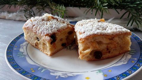 Auf einem dekorativen Teller liegen zwei Stücke Stollenkuchen, leicht bestäubt mit Puderzucker, umgeben von Tannenzweigen.