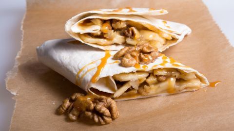 Zwei Frühstücks-Wraps mit Erdnussbutter und Walnusskernen liegen auf braunem Papier, tropfen überzogen mit gesunder Erdnusssauce.