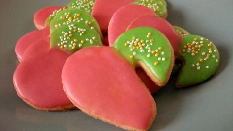 Bunte Dinkel-Tassenkekse mit pinker und grüner Zuckerglasur liegen auf einem grauen Teller und laden zum Naschen ein.