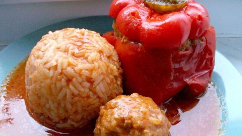 Gefüllte Paprika sitzt auf einem Teller, umgeben von Jasminreis und einer kleinen Fleischbällchen in Sauce.