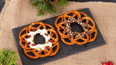 Zwei weihnachtliche Brezel-Kränze liegen auf einem schwarzen Steinplatte, dekoriert mit Zuckerguss und grünen Pistazien.