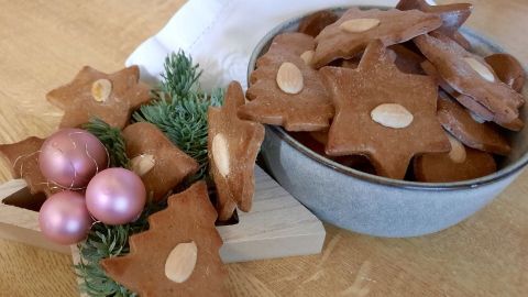 Honigplätzchen mit Mandeln liegen in einer Schüssel, umgeben von Weihnachtsdekoration wie Sternen und Kugeln.