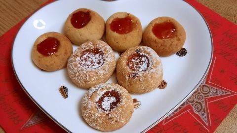 Auf einem herzförmigen Teller liegen Husarenkrapfen, gefüllt mit Marmelade, auf einem festlichen roten Untergrund.