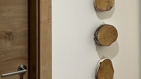 Drei Birkenscheiben hängen an einer weißen Wand neben einer Holzfarbentür und verleihen dem Raum natürlichen Charme.