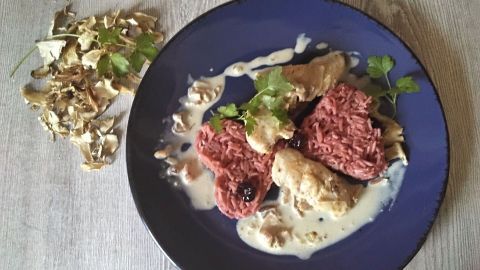 Ein Teller mit Glühwein-Basmati-Reis und Hähnchenfilet in einer cremigen Sauce, dekoriert mit frischen Kräutern.