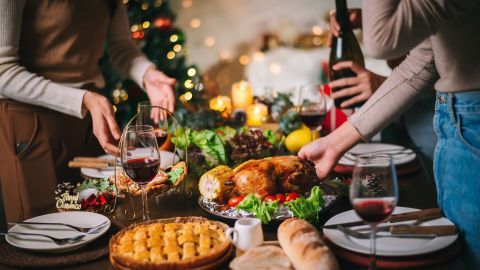 Ein festlich gedeckter Tisch wird mit einem gebratenen Hähnchen, Wein und traditionellem Weihnachtsessen vorbereitet.