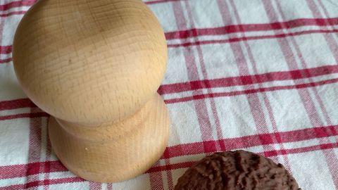 Eine Holzform steht neben einem Lebkuchenplätzchen auf einem karierten Tuch in der Küche.
