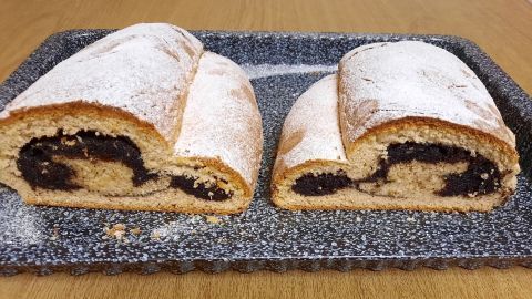 Saftiger Stollen mit Mohnfüllung liegt auf einem Blech, die geschnittenen Stücke zeigen die dunkle Füllung.