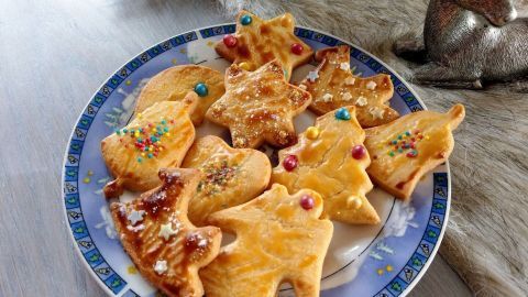 Butterplätzchen liegen auf einem Teller, bunt dekoriert und in verschiedenen Formen, umgeben von weihnachtlicher Dekoration.