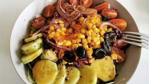 Ein bunter Salat mit Gurken, Tomaten, Mais und Oliven wird appetitlich in einer Schüssel angerichtet, um gesund zu essen.