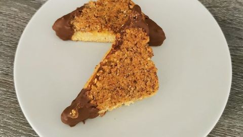 Auf einem weißen Teller liegen zwei gebackene Nussecken, die mit Schokolade überzogen sind und goldbraun aussehen.