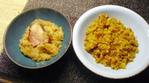 Kartoffelsterz ist in einer weißen Schüssel neben einem Teller mit Sauerkraut und Speck auf einem Tisch arrangiert.